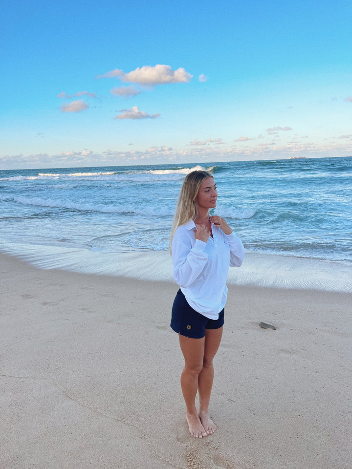 girl at beach in front of water wearing navy sol apparel training shorts for women and white sol apparel polo shirt