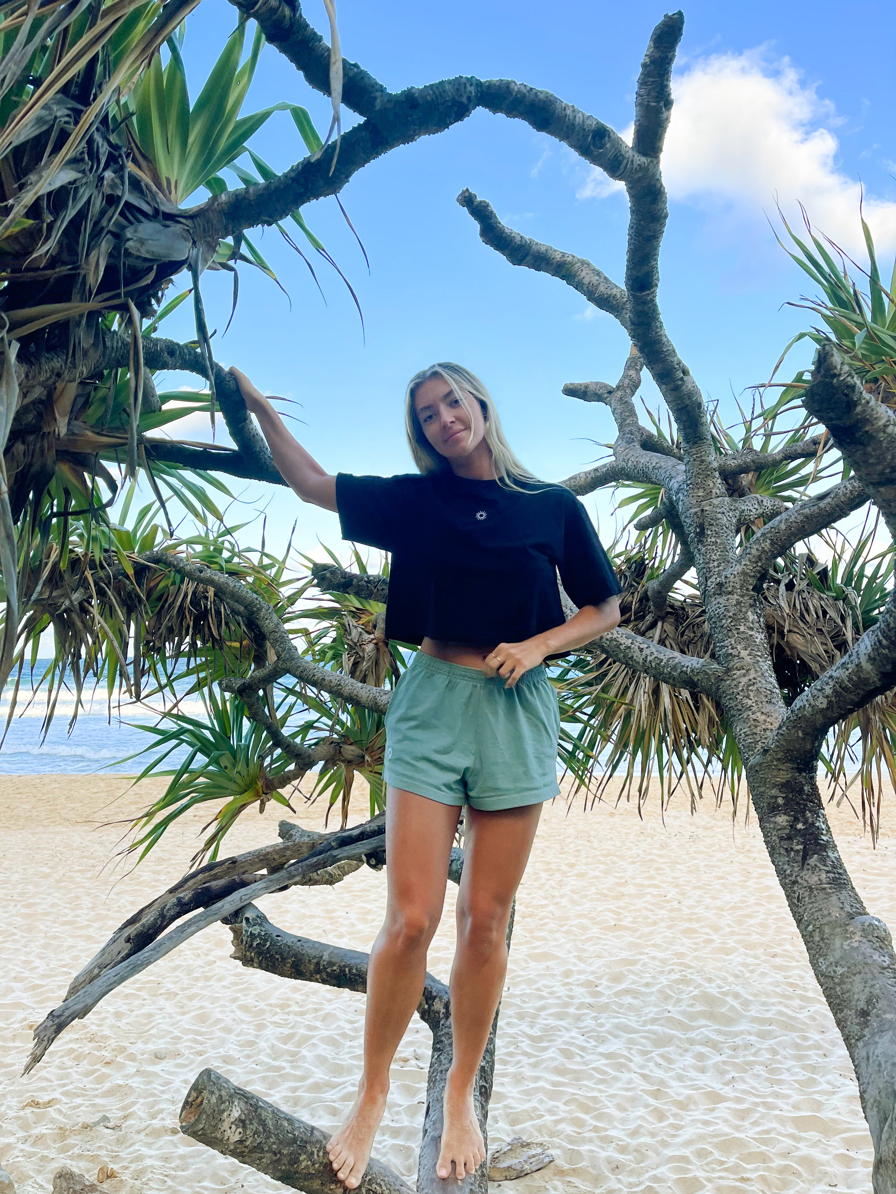 woman standing on palm tree at the beach wearing an oversized black cotton crop tee and sol apparel womens green training shorts