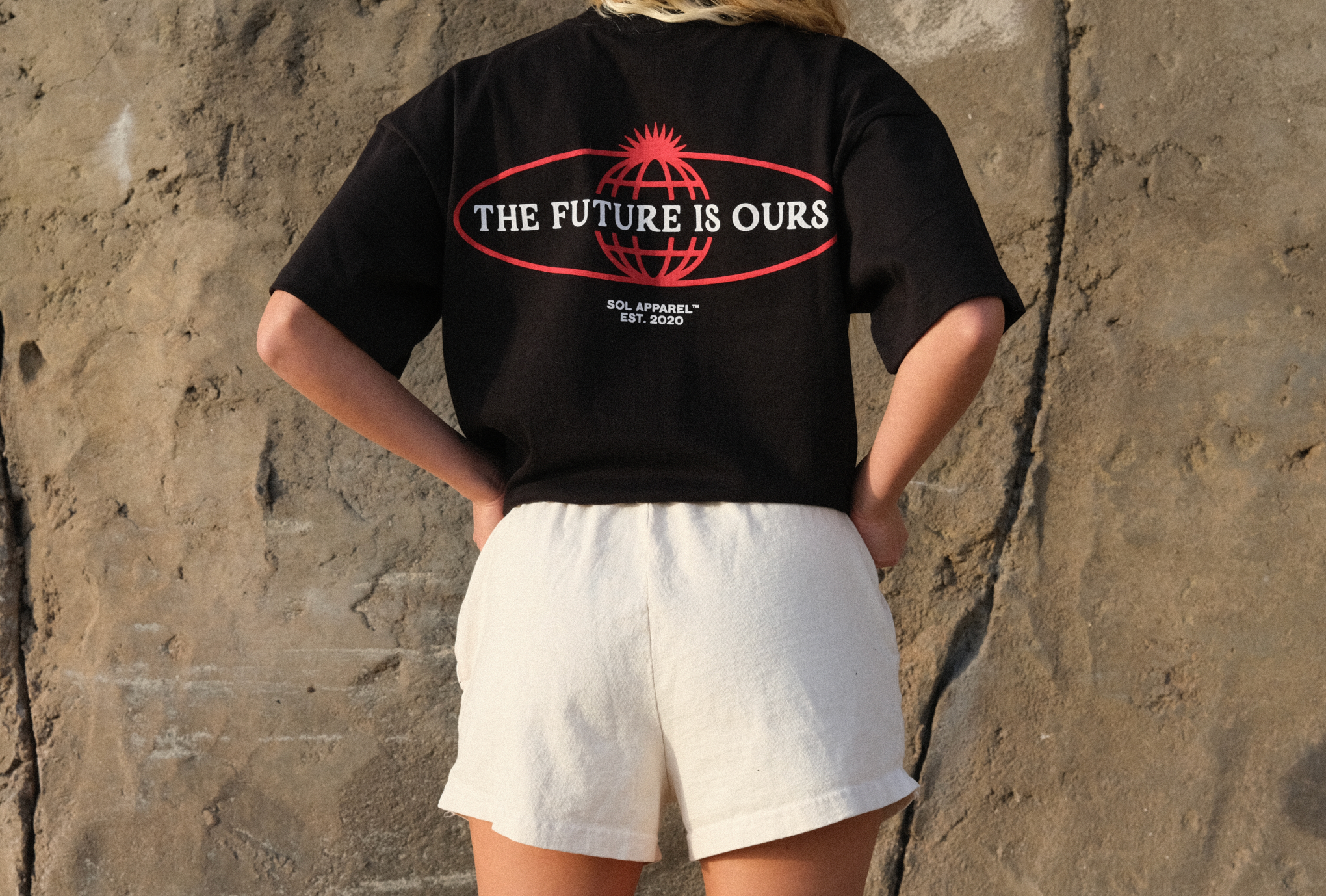 woman standing in front of beach cliff wearing cream cotton training shorts for women and a black cotton tee 