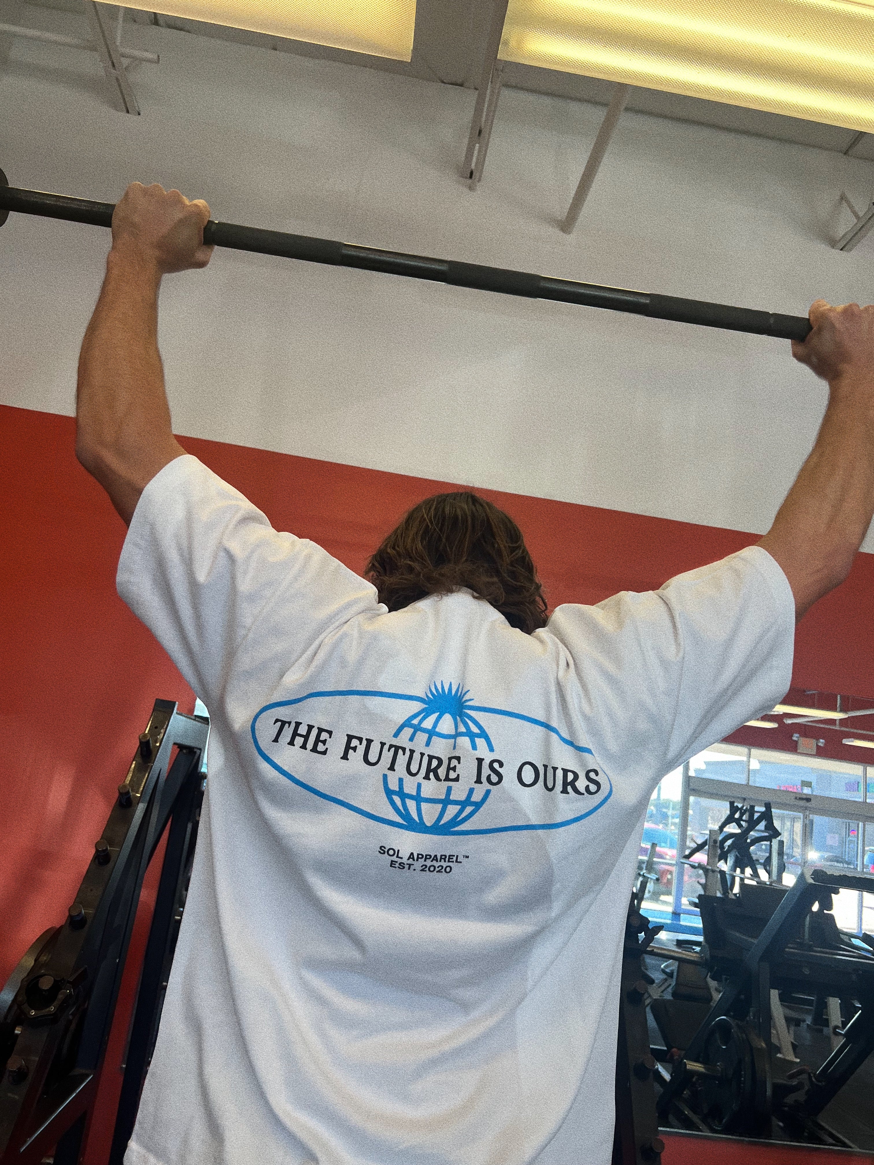 sol brah doing pull ups in the gym while wearing a white cotton tshirt that says the future is ours in black text 