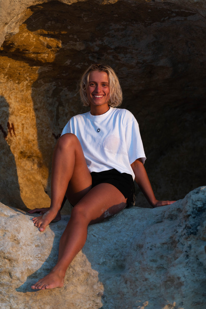 girl sittin on rocks at the beach wearing a sol apparel oversized cotton crop tee and womens black cotton training shorts